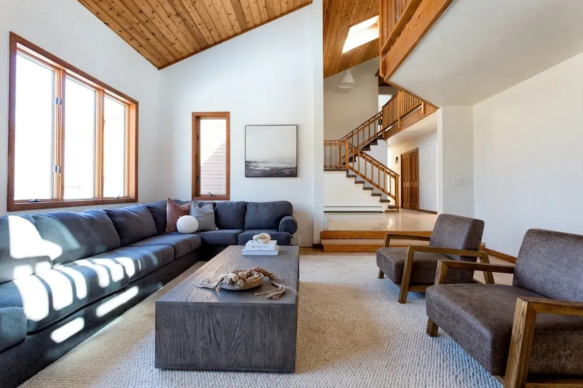 The living room: a long sectional under the cedar ceiling, the stair rising behind